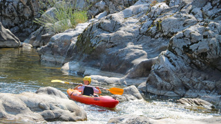 Enfant en kayak sur une rivière rocheuse au Flower Camping Mas de Champel, Auvergne-Rhône-Alpes, France.