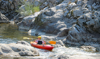 Child kayaking on a rocky river at Flower Camping Mas de Champel in Auvergne-Rhône-Alpes, France.