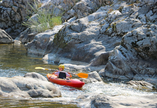 Niño en kayak en un río rocoso en Flower Camping Mas de Champel, Auvergne-Rhône-Alpes, Francia.