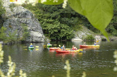 Gruppe mennesker i kajakker på en rolig flod omgivet af grønne træer og klipper i Auvergne-Rhône-Alpes.