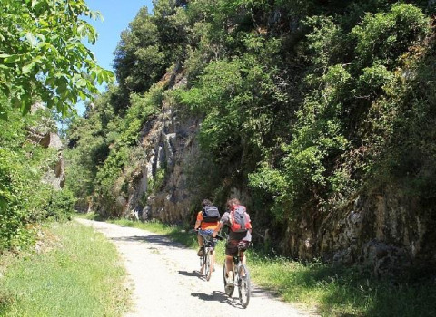 Two cyclists ride along a scenic path near Les Ollières sur Eyrieux in Auvergne-Rhône-Alpes, France, surrounded by greenery.