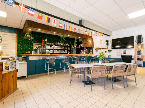 Interiør af baren på Flower Camping Les Paludiers med borde, stole, bar og flag, Pays de la Loire, Frankrig.