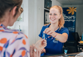 Receptioniste geeft sleutel aan gast bij Flower Camping Les Paludiers in Pays de la Loire, Frankrijk.