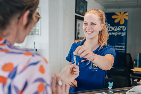 Receptionist handing a key to a guest at Flower Camping Les Paludiers in Pays de la Loire, France.