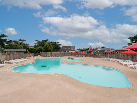 Outdoor swimming pool with white loungers and red umbrellas at Flower Camping Les Paludiers, Pays de la Loire.