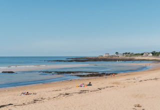 Sandy beach with scattered visitors at Flower Camping Les Paludiers in Pays de la Loire, France on a sunny day.