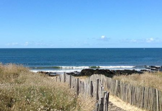 Un sendero de arena con valla de madera atraviesa las dunas hacia la playa en Flower Camping Les Paludiers, Francia.