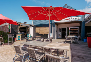 Udendørs terrasse med røde parasoller og caféborde på Flower Camping Les Paludiers i Pays de la Loire.