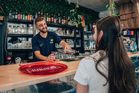 Barman serveert lachend een drankje aan een vrouw bij Flower Camping Les Paludiers in Pays de la Loire.