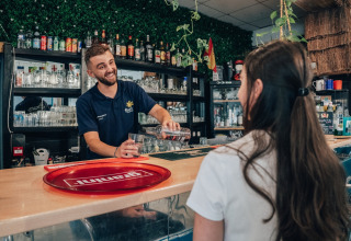 Barista sorride servendo una bevanda a una donna al bar di Flower Camping Les Paludiers in Pays de la Loire.