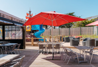 Buitenterras met rode parasols, tafels en speeltuin bij Flower Camping Les Paludiers, Pays de la Loire.