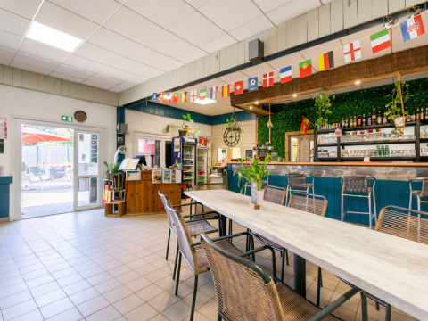 Lichte gemeenschappelijke ruimte met bar en vlaggen bij Flower Camping Les Paludiers in Pays de la Loire, Frankrijk.