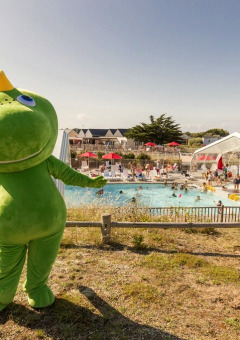 Mascotte verde davanti a una piscina affollata al Flower Camping Les Paludiers nel Pays de la Loire, Francia.