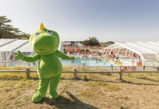 Mascotte verde davanti a una piscina affollata al Flower Camping Les Paludiers nel Pays de la Loire, Francia.
