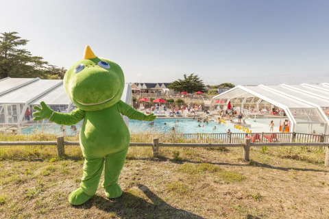 Maskottchen im grünen Kostüm steht vor dem Schwimmbad und Gästen bei Flower Camping Les Paludiers in Frankreich.