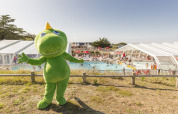 Mascotte verde davanti a una piscina affollata al Flower Camping Les Paludiers nel Pays de la Loire, Francia.
