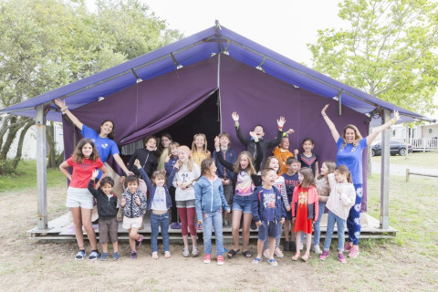Børn og voksne poserer glade foran et lilla telt på Flower Camping Les Paludiers i Pays de la Loire, Frankrig.