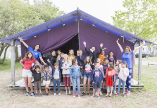 Kinder und Erwachsene feiern und posieren vor einem lila Zelt im Flower Camping Les Paludiers, Pays de la Loire, Frankreich.