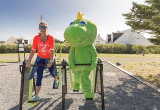 Frau und Person im grünen Dinosaurierkostüm trainieren draußen im Flower Camping Les Paludiers, Frankreich.