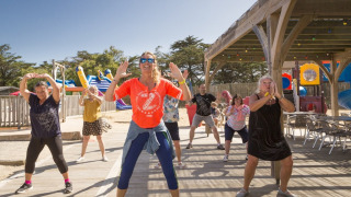 Groep volwassenen neemt deel aan een zonnige outdoor fitnessles op Flower Camping Les Paludiers, Frankrijk.
