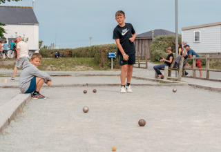 Zwei Jungen spielen Boule auf einem Schotterplatz im Flower Camping Les Paludiers in Pays de la Loire, Frankreich.