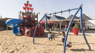 Kinderen spelen op een speeltuin met piratenschip en schommels bij Flower Camping Les Paludiers, Frankrijk.