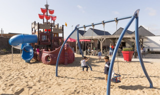 Kinder spielen auf einem Spielplatz mit Piratenschiff und Schaukeln im Flower Camping Les Paludiers, Frankreich.
