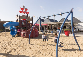 Bambini giocano su un parco giochi con nave dei pirati e altalene a Flower Camping Les Paludiers, Francia.