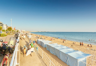 Beach view at Flower Camping Les Paludiers, Pays de la Loire, France, with striped huts and people relaxing.