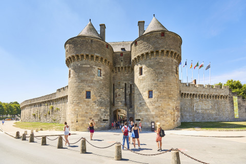 Tourists outside a historic stone castle with round towers at Flower Camping Les Paludiers, Pays de la Loire, France.