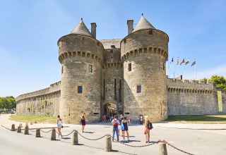 Turistas frente a un antiguo castillo de piedra con torres redondas en Flower Camping Les Paludiers, Pays de la Loire, Francia.