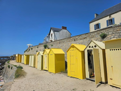 Cabine da spiaggia gialle lungo un muro di pietra al Flower Camping Les Paludiers, Pays de la Loire, Francia.