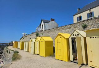 Gele strandcabines en stenen muur bij Flower Camping Les Paludiers, Pays de la Loire, Frankrijk, op een zonnige dag.