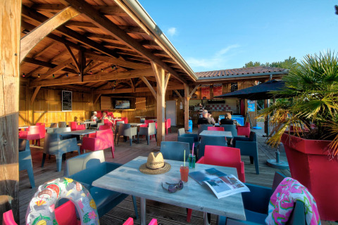 Udendørs caféområde på Flower Camping Le Bel Air i Nouvelle-Aquitaine, Frankrig, med farverige stole.