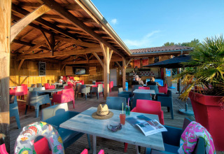 Udendørs caféområde på Flower Camping Le Bel Air i Nouvelle-Aquitaine, Frankrig, med farverige stole.
