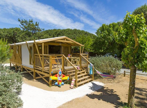 Wooden holiday cabin with toys and a hammock at Flower Camping Le Bel Air holiday park in Nouvelle-Aquitaine, France.