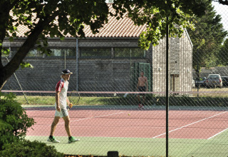 Twee mensen spelen tennis op een buitenbaan bij Flower Camping Le Bel Air in Nouvelle-Aquitaine, Frankrijk.