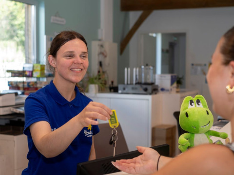 Receptionist udleverer nøgler til gæst ved Flower Camping Le Bel Air feriepark i Nouvelle-Aquitaine, Frankrig.