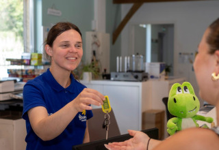 Receptionist udleverer nøgler til gæst ved Flower Camping Le Bel Air feriepark i Nouvelle-Aquitaine, Frankrig.