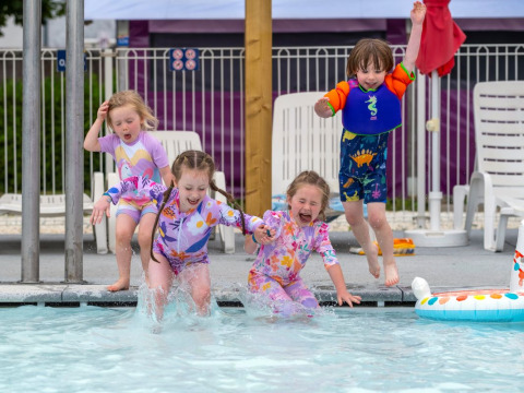 Niños saltando felices en una piscina en Flower Camping Le Bel Air, Nouvelle-Aquitaine, Francia.
