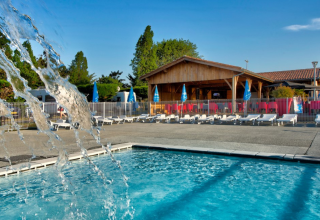 Swimming pool and sun loungers at Flower Camping Le Bel Air holiday park in Nouvelle-Aquitaine, France on a sunny day.