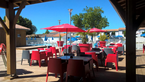 Terrasse mit roten Stühlen, Sonnenschirmen und Poolblick im Flower Camping Le Bel Air, Nouvelle-Aquitaine, Frankreich.