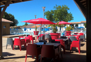 Udendørs terrasse med røde stole, parasoller og udsigt til pool i Flower Camping Le Bel Air, Nouvelle-Aquitaine.