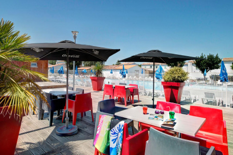 Terraza soleada con sillas coloridas, sombrillas y vista a la piscina en Flower Camping Le Bel Air, Francia.