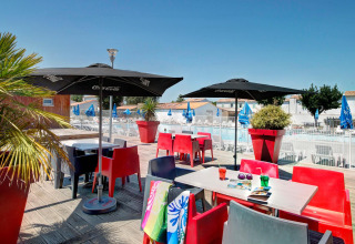 Terrasse ensoleillée avec chaises colorées, parasols et vue sur la piscine au Flower Camping Le Bel Air.