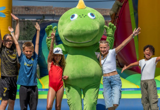 Kinderen staan met een groene dinosaurusmascotte op het springkasteel bij Flower Camping Le Bel Air, Frankrijk.