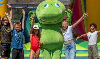 Kinder posieren mit einem grünen Dinosauriermaskottchen auf einer Hüpfburg in Flower Camping Le Bel Air.