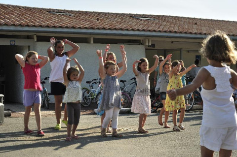 Kinder tanzen und spielen draußen bei sonnigem Wetter im Flower Camping Le Bel Air in Nouvelle-Aquitaine, Frankreich.