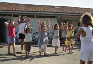 Børn leger og danser udendørs i solskin ved Flower Camping Le Bel Air i Nouvelle-Aquitaine, Frankrig.