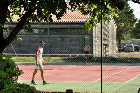 To personer spiller tennis på en udendørs bane omgivet af træer ved Flower Camping Le Bel Air i Frankrig.